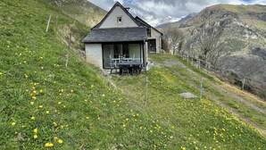 A stone house with a sloped roof, a small porch, and a table and chairs outside.