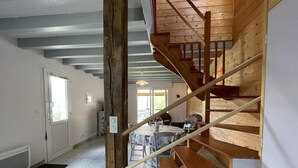 A wooden staircase leading to a second floor, a dining area with a table and chairs, and a view of the outdoors through a window.