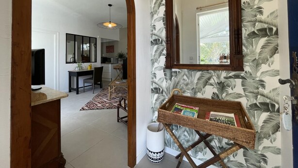 A hallway with a wooden archway leading to a dining area with a table and chairs, a kitchen in the background, and a large mirror on the wall.
