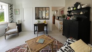 A modern living room with a dining area, a black cabinet with decorative items, and a large window with curtains.