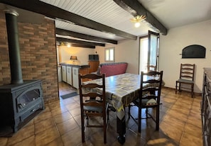 A cozy room with a fireplace, a dining table with chairs, a kitchen area, and a window with blinds.