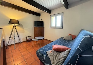 A room with a blue sofa, a small table, a lamp, a TV, and a window.