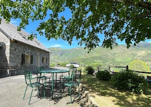 Un bâtiment en pierre avec une table et des chaises dans un jardin, offrant une vue sur un paysage montagneux.