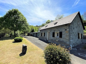 A stone building with a sloped roof, surrounded by a grassy area with trees and a stone path.