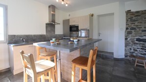Una cocina moderna con una isla central, sillas de madera y una pared de piedra.