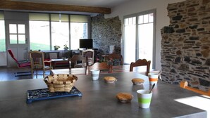 Amplia sala de estar con pared de piedra, una mesa de comedor con sillas y un televisor al fondo.