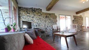 Una sala de estar con una pared de piedra, un sofá rojo, una mesa de madera y un televisor.