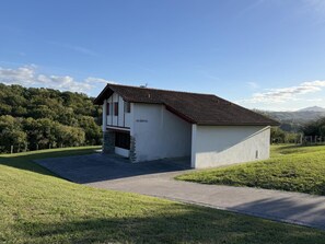 Un bâtiment à deux étages, doté de fondations en pierre et d’un toit en pente, entouré d’une pelouse et d’arbres.