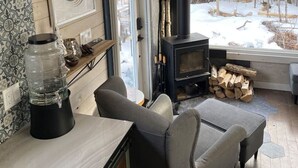 A cozy living room with a fireplace, a large window, and a view of the snowy outdoors.