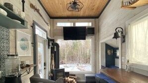 A modern kitchen with wooden ceiling, a built-in TV, and a large window overlooking a snowy landscape.