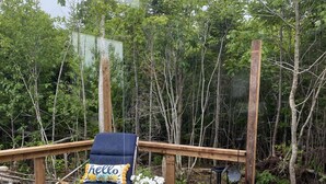 A wooden deck with a hot tub, a blue lounge chair with a 'hello' pillow, and potted plants.