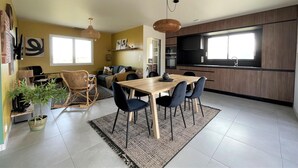 Eine moderne Küche mit Holzausstattung, ein Essbereich mit Tisch und Stühlen sowie ein Wohnbereich mit Sofa und Couchtisch.
