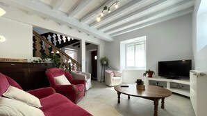 A living room with a red sofa, a wooden coffee table, and a TV. There's a staircase with a wooden railing and a potted plant. - Etchechoury - Moncayolle Larrory Mendibieu (MONCAYOLLE LARRORY MENDIBIEU)