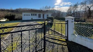 Un edificio bianco con tetto in tegole, vialetto sterrato e cancello in metallo.