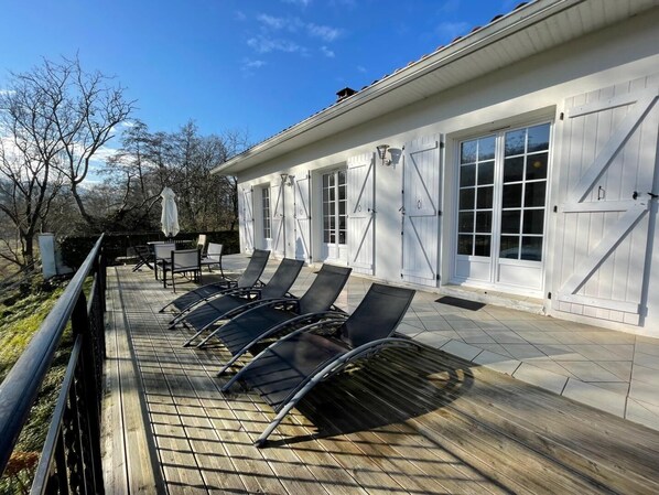 A covered outdoor deck with lounge chairs, a table, and umbrellas. - Geriza - Uhart-cize - Gîte (UHART-CIZE)
