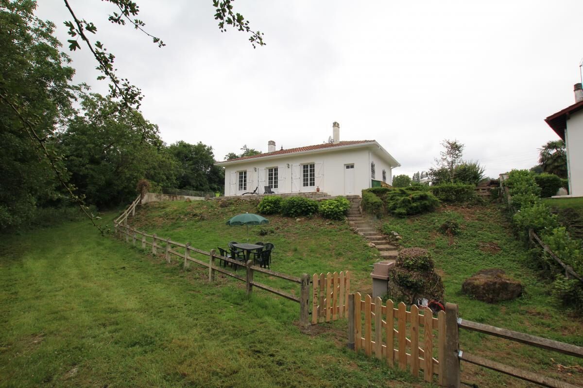 A white house with a red-tiled roof, a wooden fence, and a green umbrella.