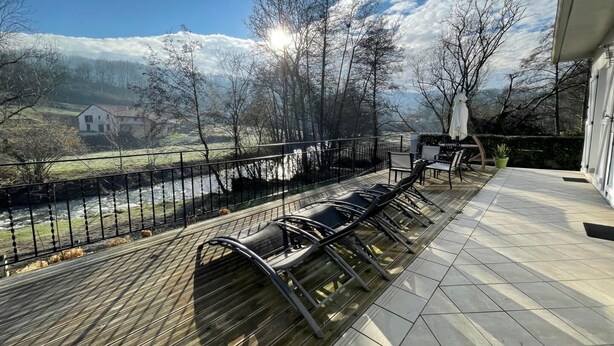 Una terrazza con posti a sedere all'aperto, vista su un fiume e una casa sullo sfondo.