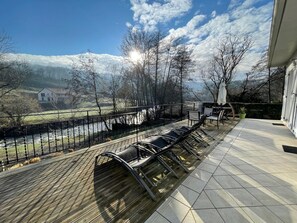 A deck with outdoor seating, a view of a river, and a house in the background. - Geriza - Uhart-cize - Gîte (UHART-CIZE)