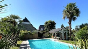 A swimming pool surrounded by palm trees and a stone building with a sloped roof. - CHEZ CASTAGNET - ASSAT (ASSAT)