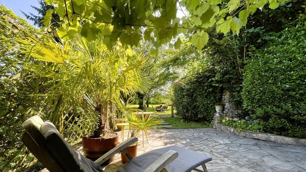 A garden patio with a lounge chair, potted plants, and a stone pathway. - CHEZ CASTAGNET - ASSAT (ASSAT)