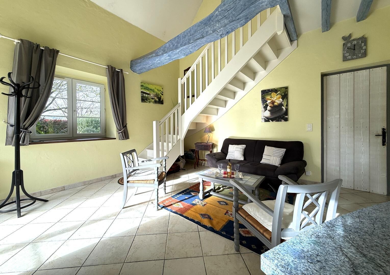 A spacious living room with a staircase, a dining area, and a large window with curtains.