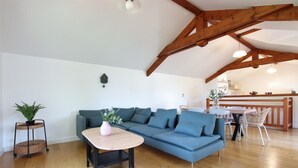 Una sala moderna con un sofá azul, una mesa de centro de madera y una zona de comedor con baranda de madera.