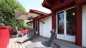 Una terraza de madera con una mesa y sillas, baranda roja y una puerta corrediza de vidrio.