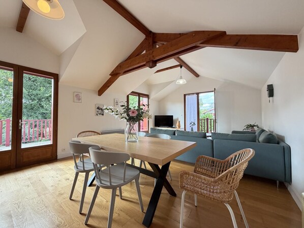 A dining area with a wooden table and chairs, a sofa, and a television in a living room.