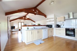 A spacious kitchen with wooden beams, white cabinets, a dishwasher, a microwave, and an oven.