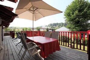 Une terrasse en bois avec une table et des chaises, un grand parasol et une rambarde rouge.