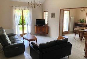 A living room with a sofa, a small table, a TV, and a cabinet. There is a door leading to a dining area with a table and chairs. - Beratarbide - Laroin (LAROIN)