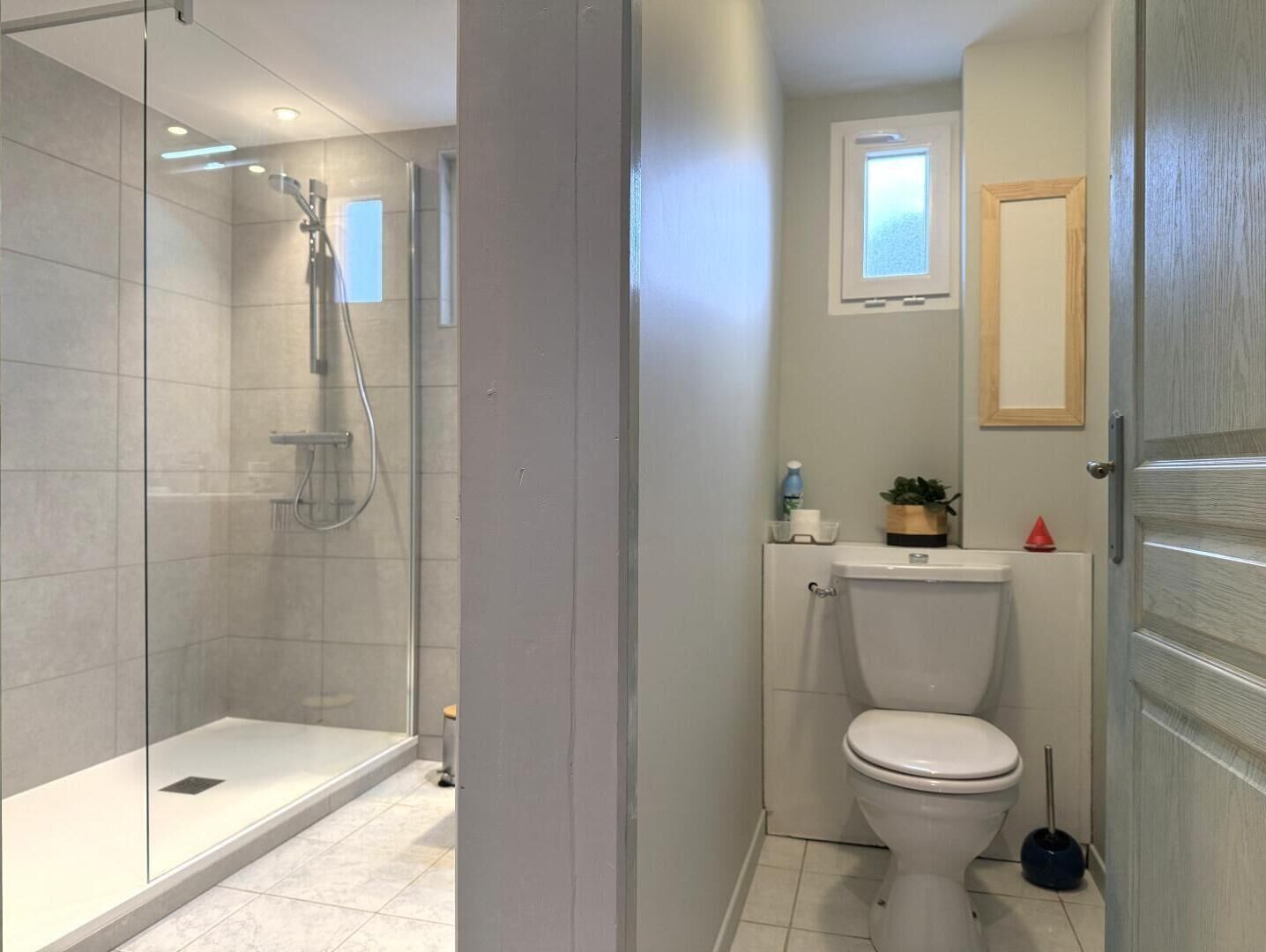 A bathroom with a glass-enclosed shower, a toilet, and a small window above the toilet.