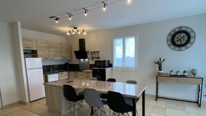 A modern kitchen with a central island, black chairs, and a dining table. There is a clock on the wall and a small plant on a console table. - Maliania - Arbonne - Gîte (ARBONNE)