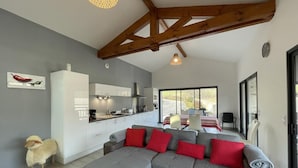 A modern living room with a grey sectional sofa, red cushions, a small white cabinet, and a wooden ceiling beam. - Buztingorria - Macaye (MACAYE)
