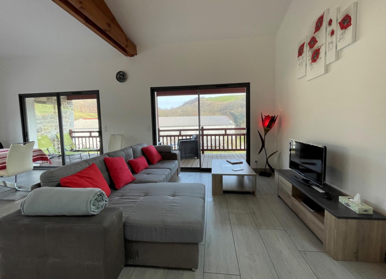 Een moderne woonkamer met een grijze bank, rode kussens, een flatscreen-tv en een balkon met uitzicht op het landschap.