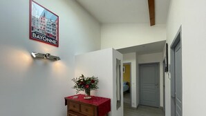 A hallway with a wooden cabinet, a vase with flowers, and a framed sign on the wall. - Buztingorria - Macaye (MACAYE)