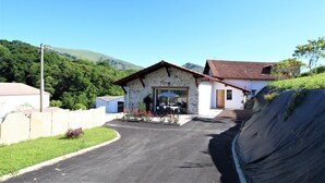 A stone building with a red-tiled roof, a paved driveway, and a hillside backdrop. - Buztingorria - Macaye (MACAYE)