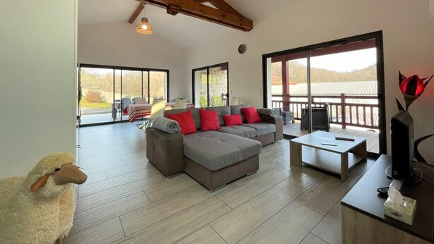 A spacious living area with a sofa, a coffee table, and a TV. There are large windows and a balcony with a view. - Buztingorria - Macaye (MACAYE)