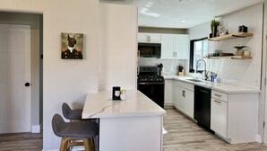 Una cocina moderna con armarios blancos, encimera de mármol y una zona de comedor con taburetes.