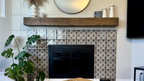 Una sala de estar moderna con chimenea, un espejo redondo y una mesa de centro de madera con libros.