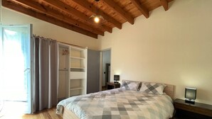 Une chambre avec un grand lit, des poutres apparentes en bois au plafond, une armoire et une table de chevet avec une lampe.