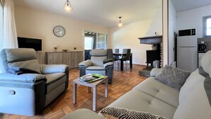 Un salon comprenant un canapé, deux fauteuils, une table basse, une table à manger avec des chaises, un téléviseur, une horloge et une cheminée.