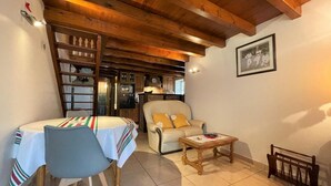 A cozy living room with a dining table, chairs, a sofa, and a small wooden coffee table. - Larzabalea - Sare - Gîte (SARE)
