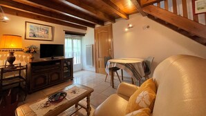 A cozy living room with a wooden ceiling, a television, a sofa, and a dining area with a table and chairs. - Larzabalea - Sare - Gîte (SARE)