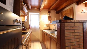 A narrow kitchen with wooden cabinets, a brick backsplash, and a stainless steel refrigerator. - Larzabalea - Sare - Gîte (SARE)