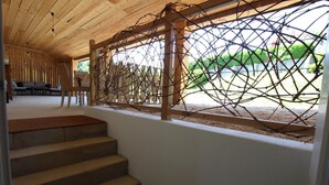 Eine Treppe führt zu einem überdachten Außenbereich mit Holzboden und einem dekorativen Zaun aus verschlungenen Ästen.