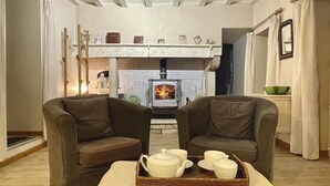 Ein gemütliches Wohnzimmer mit Kamin, zwei Sesseln, einem kleinen Tisch mit Teeservice und einem dekorativen Kaminvorsatz.