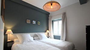 Ein Schlafzimmer mit zwei Betten, einem fensterbelaubten Fenster und einer Wandlampe.