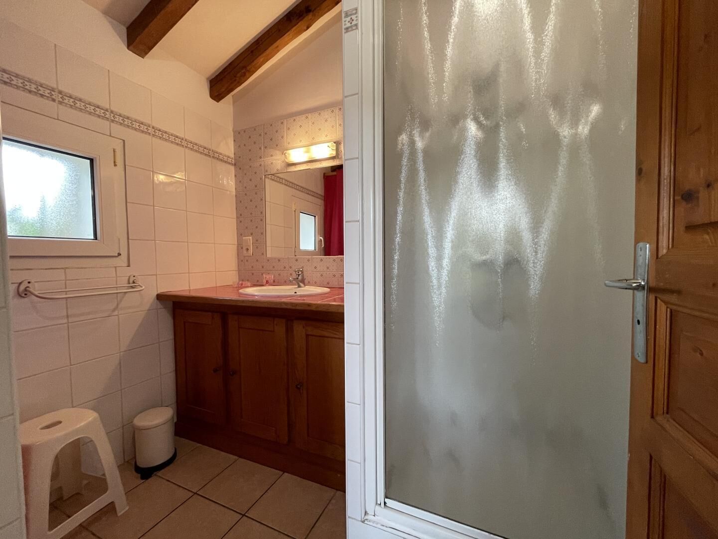 A bathroom with a window, a sink, a mirror, and wooden cabinets.