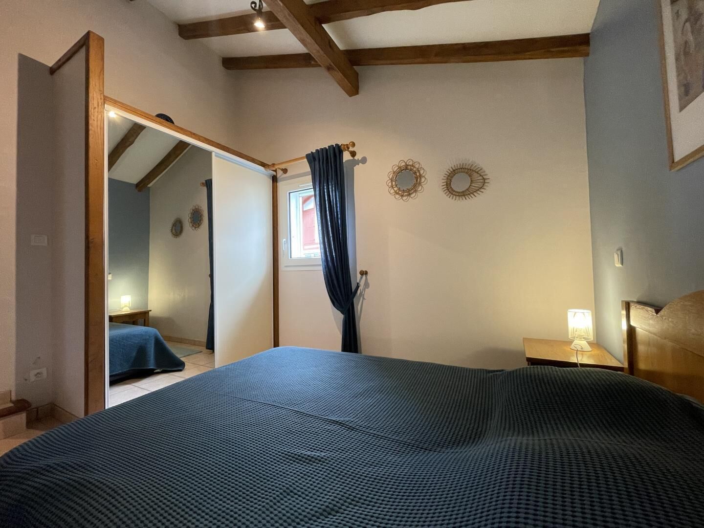 Une chambre à coucher avec un grand lit, une table de chevet avec une lampe, un miroir et une fenêtre avec des rideaux.